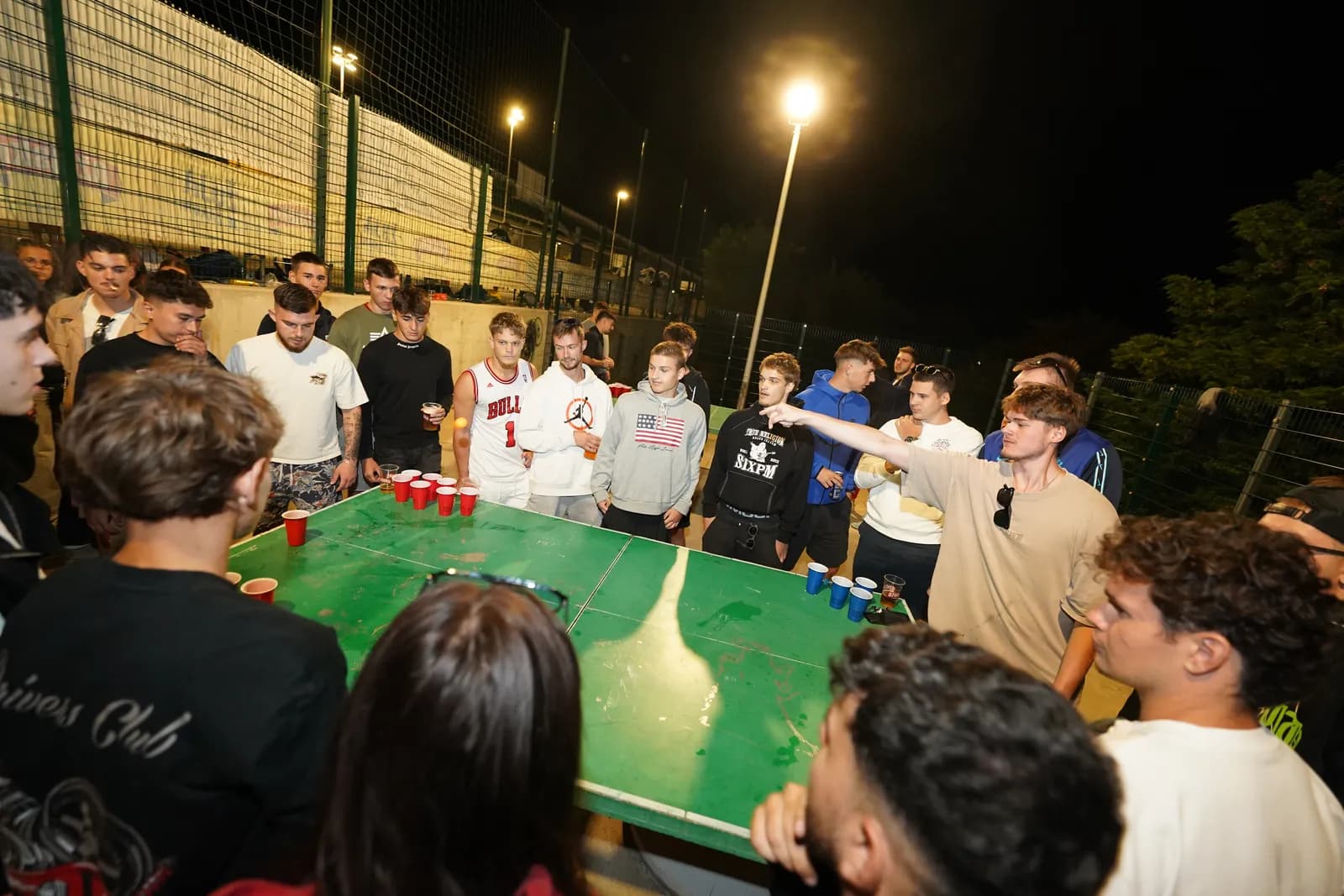 Beerpong stol s crvenim čašama okružen igračima